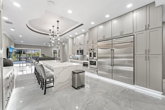 kitchen featuring a tray ceiling, stainless steel appliances, marble finish floor, and open floor plan