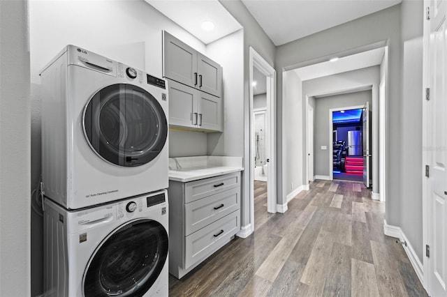 washroom featuring stacked washer / drying machine, cabinet space, baseboards, and wood finished floors