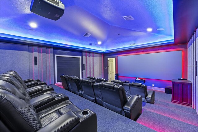 cinema room with carpet flooring, lofted ceiling, a raised ceiling, and visible vents