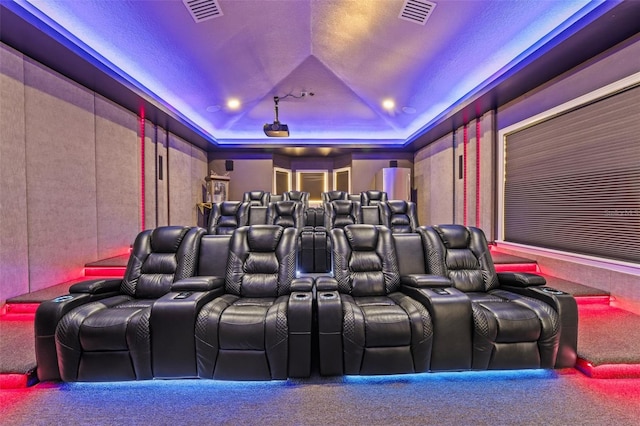 home theater featuring a raised ceiling, carpet flooring, visible vents, and vaulted ceiling