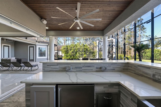 view of patio / terrace featuring an outdoor living space, glass enclosure, outdoor wet bar, an outdoor kitchen, and a ceiling fan