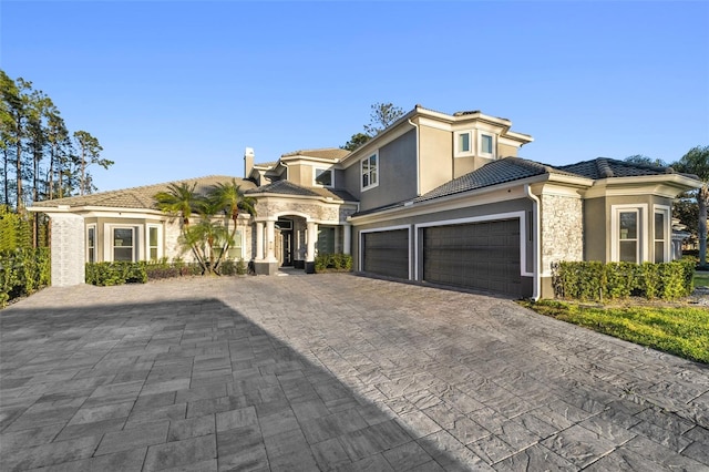 view of front of home with a tile roof, stucco siding, decorative driveway, stone siding, and an attached garage