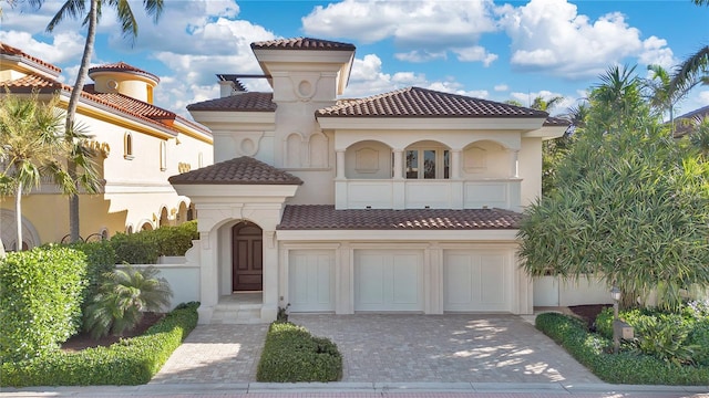 mediterranean / spanish house with stucco siding, a tiled roof, decorative driveway, and a balcony