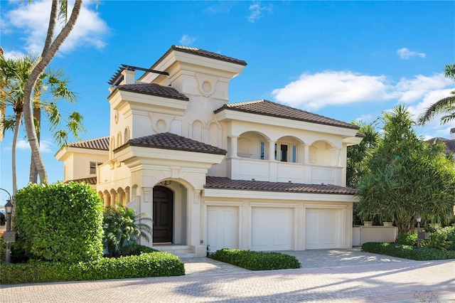 mediterranean / spanish home featuring stucco siding, a tile roof, decorative driveway, an attached garage, and a balcony