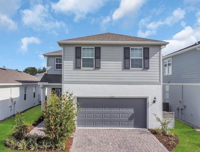 traditional-style house featuring cooling unit, a garage, stucco siding, and decorative driveway