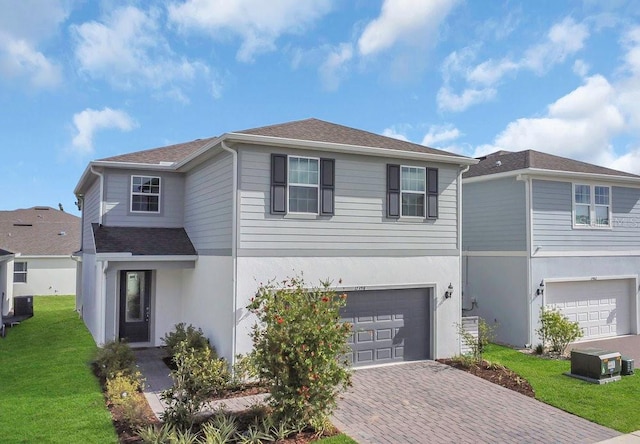 traditional-style home with a garage, central air condition unit, decorative driveway, a front yard, and a shingled roof