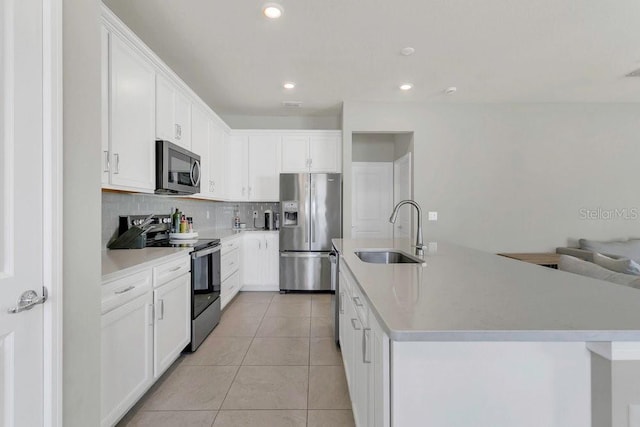 kitchen featuring tasteful backsplash, light tile patterned floors, a sink, appliances with stainless steel finishes, and a center island with sink