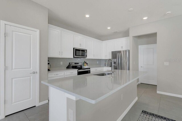 kitchen with backsplash, light tile patterned flooring, white cabinets, appliances with stainless steel finishes, and a sink