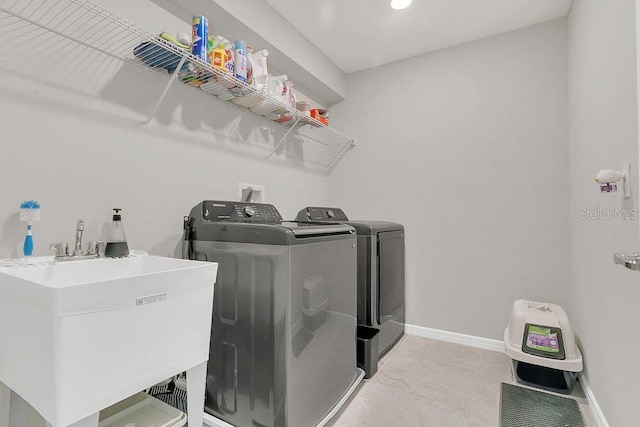clothes washing area with a sink, baseboards, separate washer and dryer, and laundry area