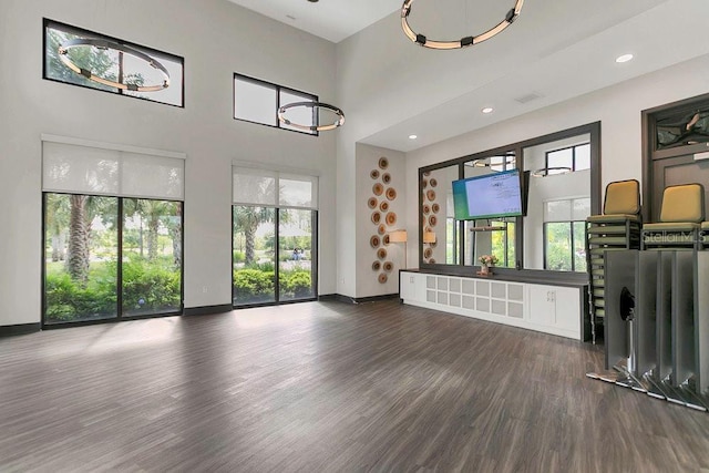 unfurnished living room with baseboards, recessed lighting, a high ceiling, and wood finished floors