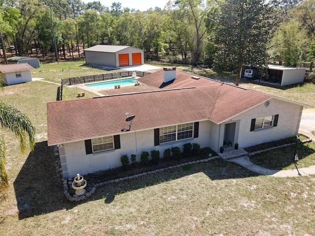 view of front of home with a shingled roof, a front lawn, stucco siding, an outbuilding, and an outdoor pool