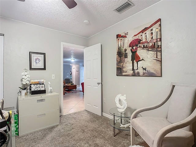 living area with visible vents, a textured ceiling, carpet, and a ceiling fan