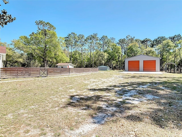 view of yard featuring fence, an outdoor structure, a garage, an outbuilding, and driveway