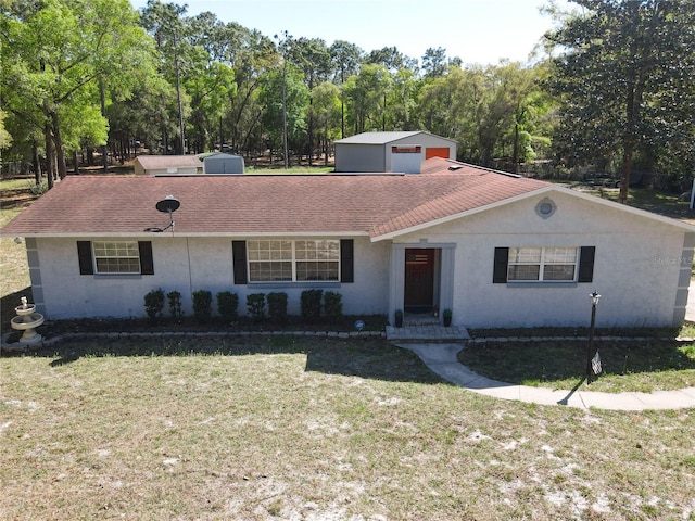 single story home featuring a front yard, an outdoor structure, roof with shingles, and stucco siding