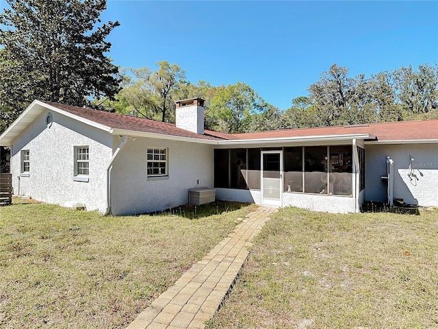 rear view of property with stucco siding, a yard, a sunroom, and a chimney