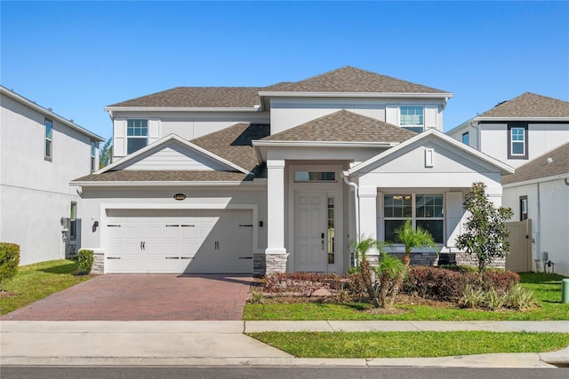 view of front of house featuring an attached garage, a shingled roof, stucco siding, stone siding, and decorative driveway