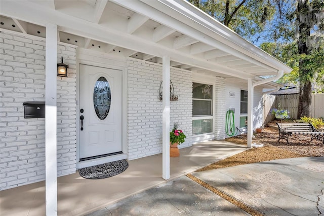 doorway to property featuring a porch, fence, and brick siding