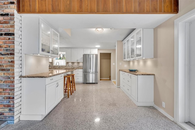 kitchen with dark stone counters, glass insert cabinets, baseboards, and freestanding refrigerator