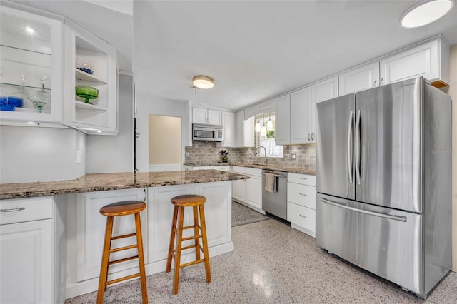 kitchen featuring a sink, stone countertops, appliances with stainless steel finishes, a breakfast bar area, and white cabinets