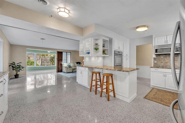 kitchen with stone counters, appliances with stainless steel finishes, light speckled floor, white cabinetry, and open shelves