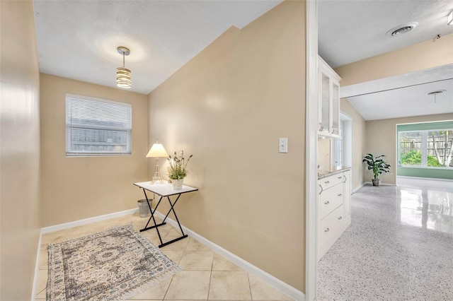 hall featuring visible vents, baseboards, and light tile patterned flooring