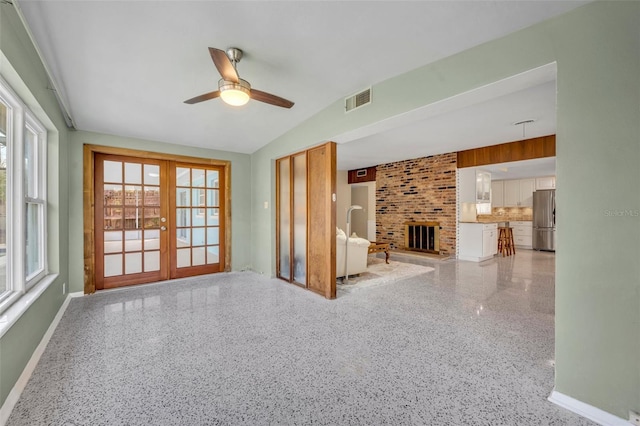 unfurnished living room with visible vents, lofted ceiling, a fireplace, french doors, and light speckled floor