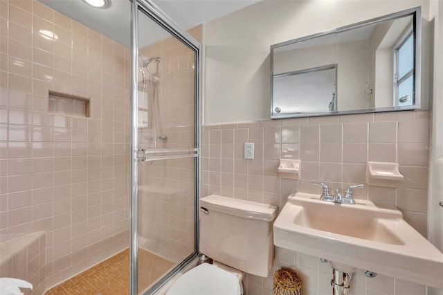 bathroom with a sink, toilet, tile walls, and a stall shower