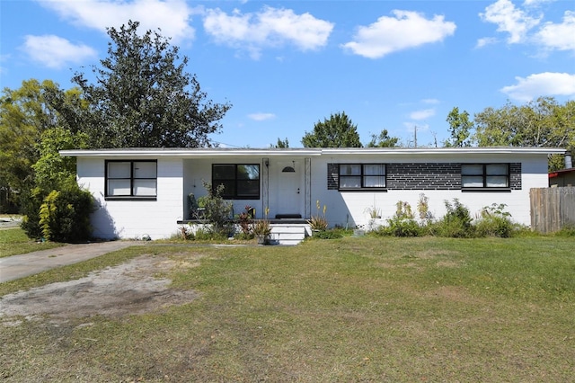 view of front facade featuring concrete block siding, fence, and a front lawn