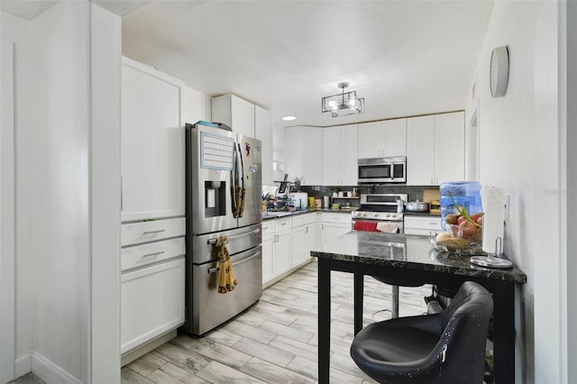 kitchen with dark countertops, backsplash, light wood-style flooring, stainless steel appliances, and white cabinetry