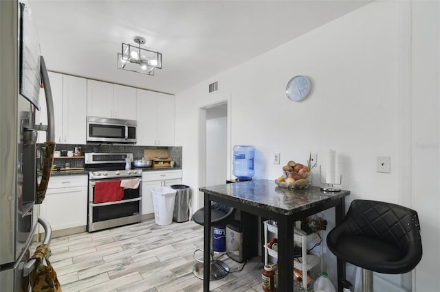 kitchen featuring visible vents, stainless steel appliances, white cabinets, dark countertops, and tasteful backsplash