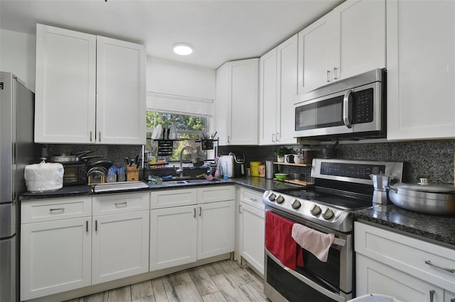 kitchen featuring backsplash, stainless steel appliances, light wood-style floors, white cabinetry, and a sink