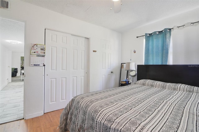 bedroom with light wood finished floors, visible vents, ceiling fan, a closet, and a textured ceiling