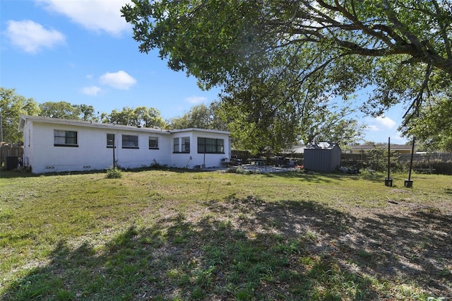 back of property with fence, a shed, a yard, crawl space, and an outbuilding