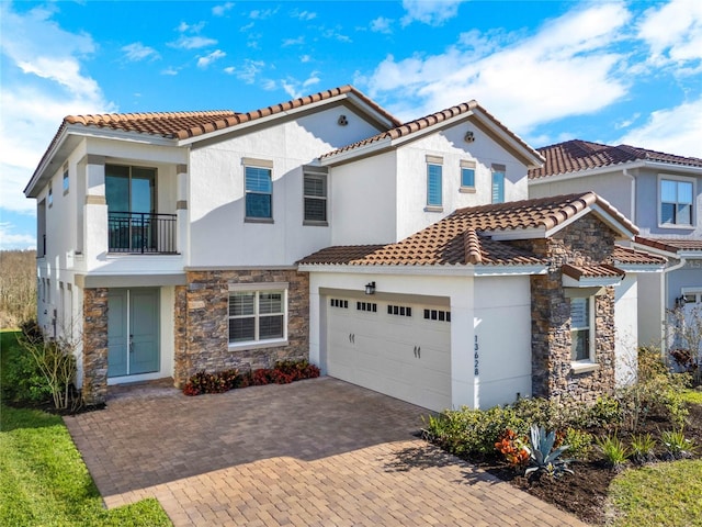 mediterranean / spanish-style house featuring a balcony, an attached garage, stucco siding, stone siding, and decorative driveway