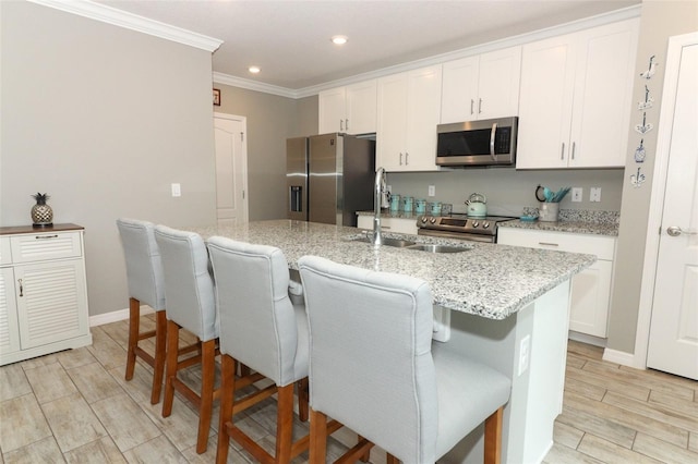 kitchen with ornamental molding, appliances with stainless steel finishes, a kitchen breakfast bar, white cabinets, and a sink