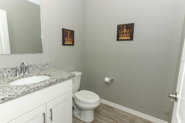 half bathroom featuring toilet, vanity, baseboards, and wood finished floors