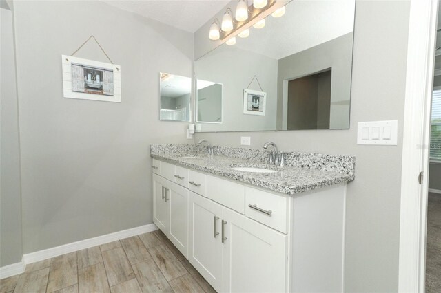 full bathroom featuring double vanity, wood finished floors, baseboards, and a sink