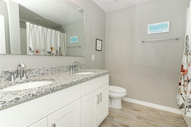 bathroom featuring toilet, wood finished floors, baseboards, and a sink