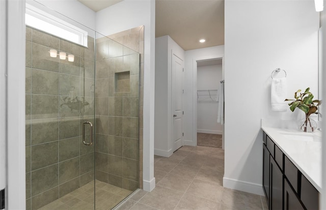 full bathroom featuring vanity, baseboards, a stall shower, a walk in closet, and tile patterned floors