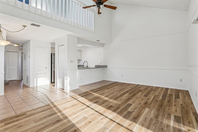 unfurnished living room with visible vents, light wood-style flooring, a towering ceiling, and a sink