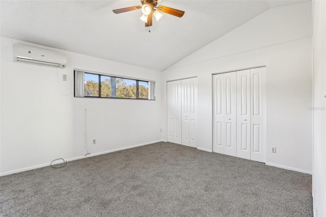 unfurnished bedroom with baseboards, carpet, multiple closets, an AC wall unit, and vaulted ceiling