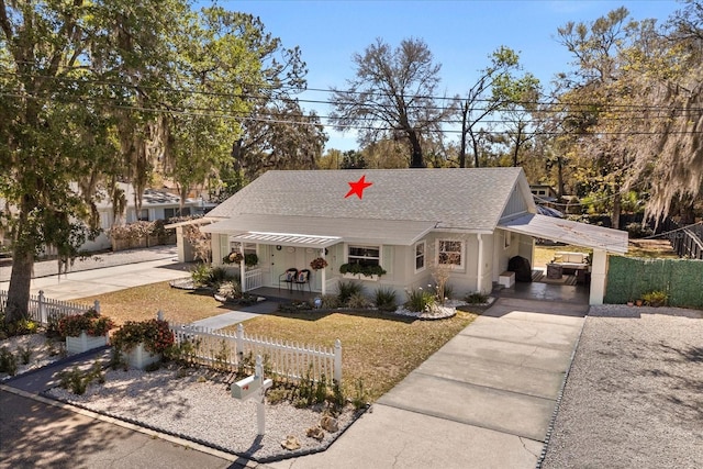 view of front of home with covered porch, a shingled roof, a carport, concrete driveway, and a fenced front yard