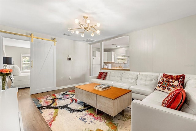 living area with an inviting chandelier, a barn door, wood finished floors, and visible vents