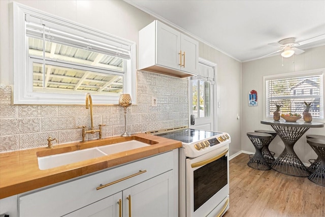 kitchen with electric range, a sink, tasteful backsplash, butcher block counters, and light wood finished floors