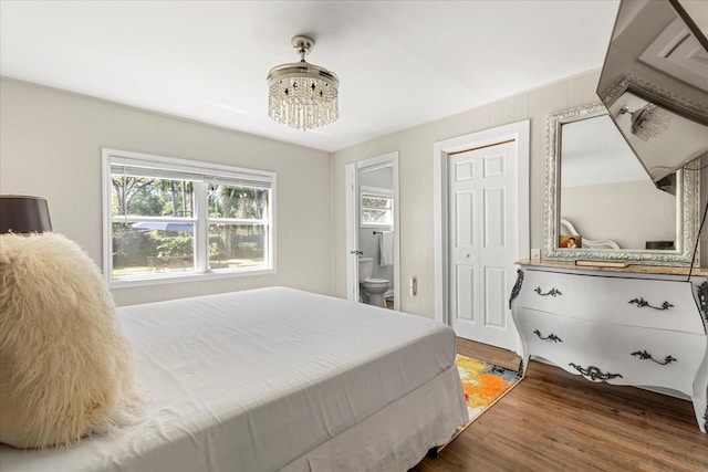 bedroom with a notable chandelier, wood finished floors, and connected bathroom