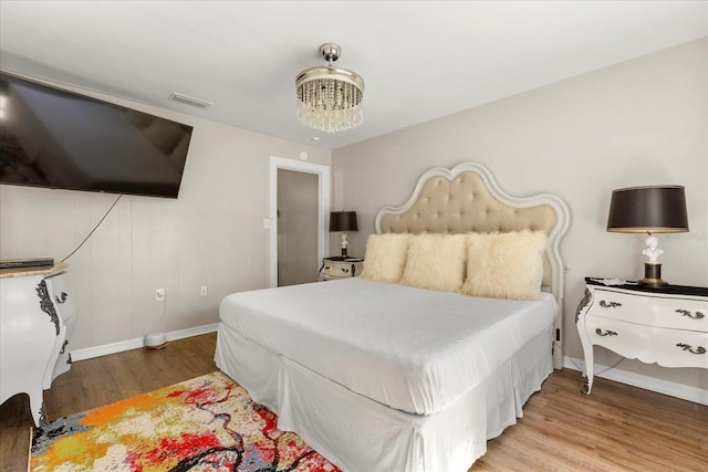 bedroom with visible vents, baseboards, an inviting chandelier, and wood finished floors