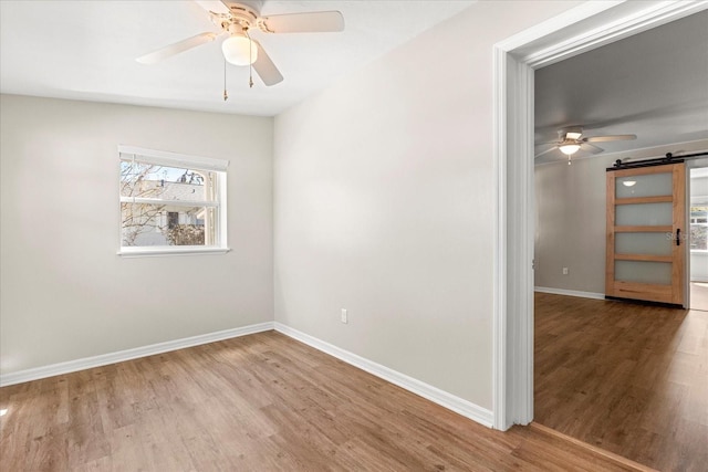 unfurnished room with a barn door, wood finished floors, baseboards, and ceiling fan