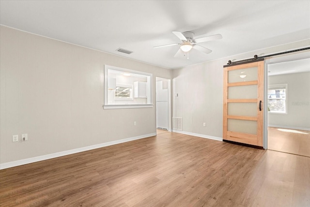 empty room with visible vents, a barn door, and wood finished floors