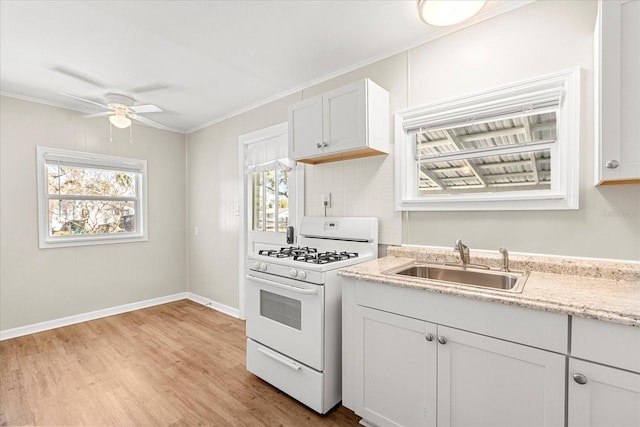 kitchen with ceiling fan, light wood-type flooring, ornamental molding, white gas range oven, and a sink