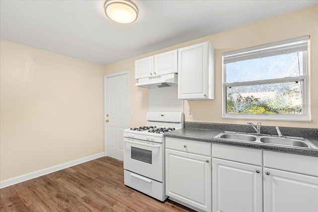 kitchen with under cabinet range hood, a sink, gas range gas stove, dark countertops, and white cabinetry